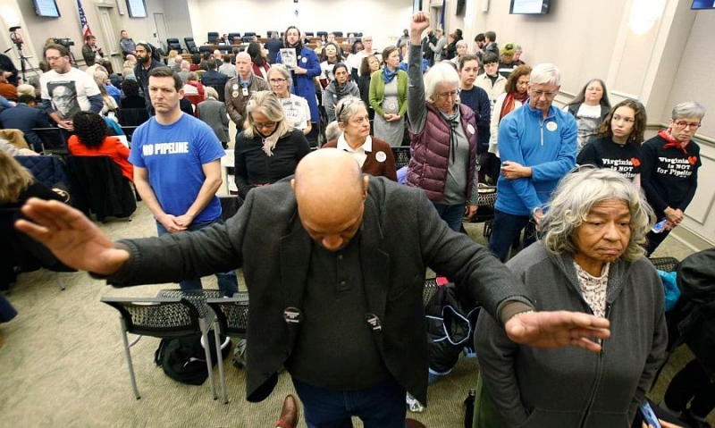 Richard Walker, an Atlantic Coast Pipeline opponent, raises his hands as he and other pipeline opponents turn their backs on a Dec. 19 meeting of a Virginia air pollution panel, which delayed a vote on a key permit for the Atlantic Coast Pipeline. 